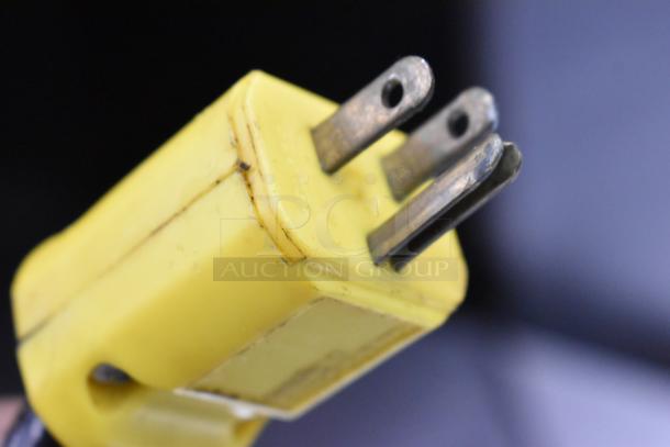 A close-up of a yellow electrical plug with three prongs, showing slight wear.