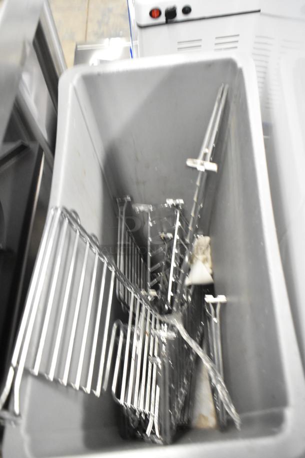 Gray Poly Slim Jim trash can with metal rack contents. Some wear visible. Ideal for industrial use.