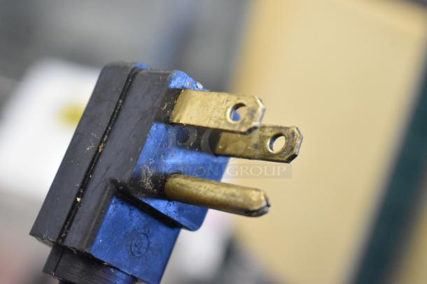 Close-up of a three-prong electrical plug, part of the Global Metal Commercial Chest Freezer. Some signs of use are visible.