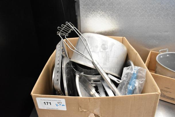 Cardboard box with assorted kitchen items including metal pots, utensils, and serving tools, all in used condition.
