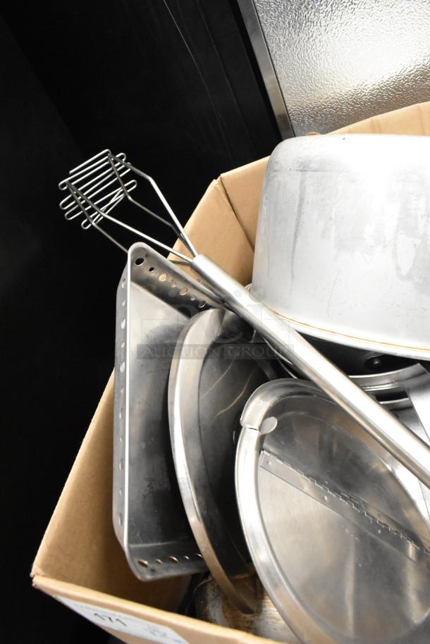 Lot of kitchen items including stainless steel utensils, sauce pots, and trays in a cardboard box. Signs of wear noted.