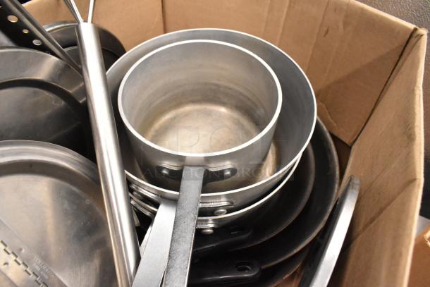 Lot of kitchen items including stainless steel utensils and sauce pots, in used condition, contained in a cardboard box.
