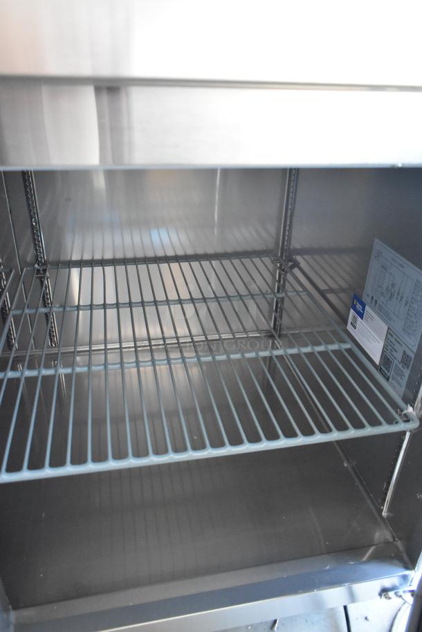 Brand new Avantco 178SSPPT3 stainless steel pizza prep table, commercial casters, visible interior shelves, minor scratches.