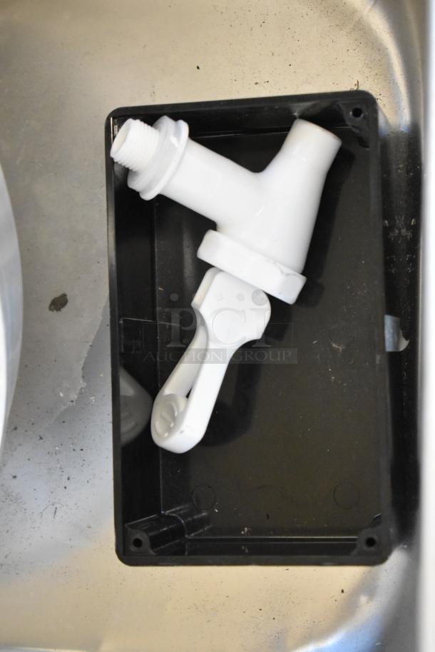 White plastic spout in a black tray on a metal surface, part of a scratch and dent auction lot.
