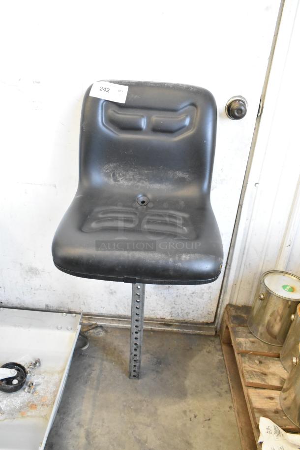 Black forklift seat with mounting post, slight wear visible. Tag marked "242" attached. Suitable for industrial use.