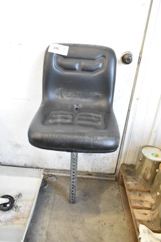 Black forklift seat with mounting post, slight wear visible. Tag marked "242" attached. Suitable for industrial use.