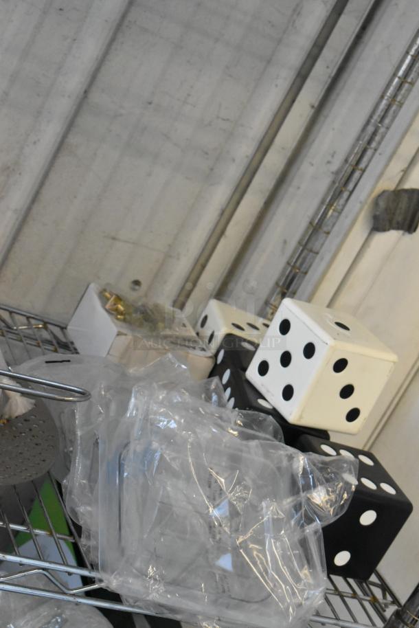 Tier lot of various items including large black and white dice, packaged serving tongs, and metal pieces on a shelf.