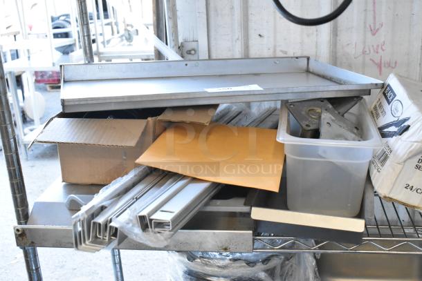 A lot containing various items: metal pieces, commercial casters, a box with contents, and an envelope on metal shelves.