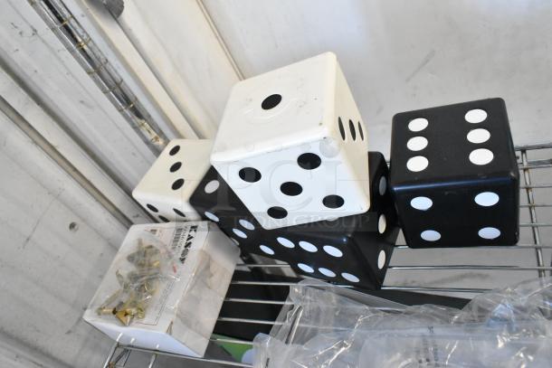 Tier lot of oversized black and white dice, commercial casters in packaging, on metal shelf. Mixed condition.
