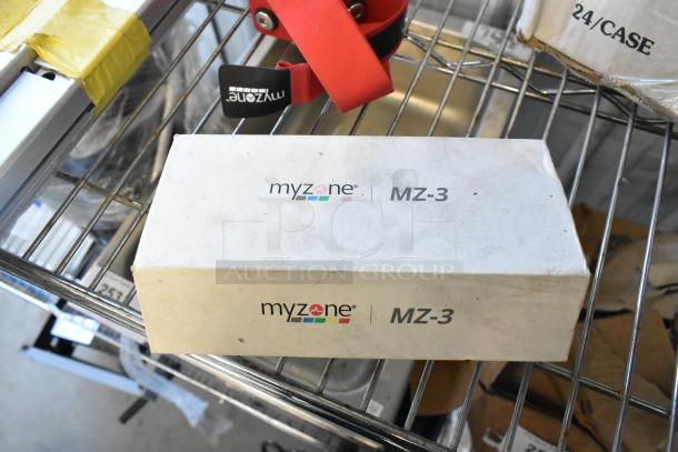 MyZone MZ-3 band box on metal shelf, slight wear visible. Includes various items like dice and serving tongs in lot.