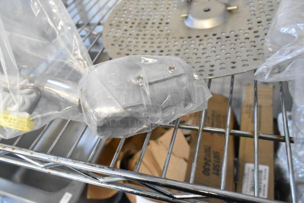 Assorted auction items including metal components, commercial casters, and more on a shelf. Items are in plastic bags.