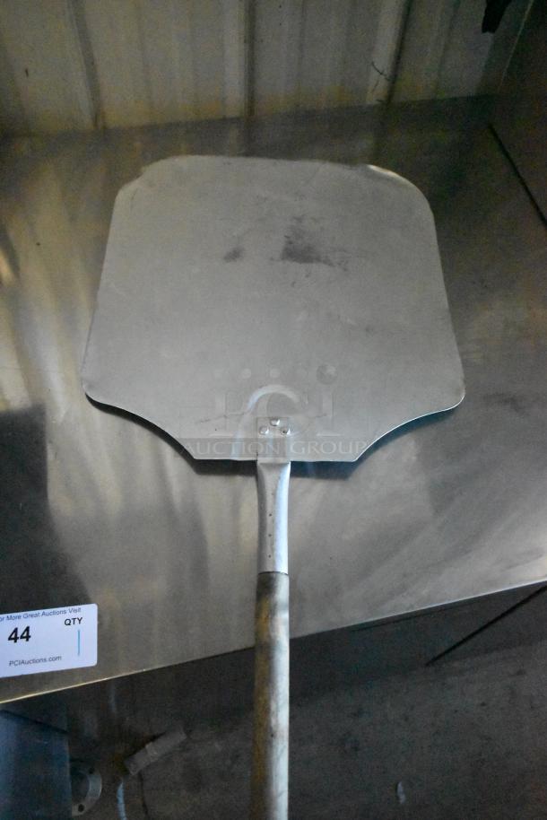 Metal pizza peel with long handle on metal surface, labeled "44 QTY." Used condition. Part of 8-item auction lot.