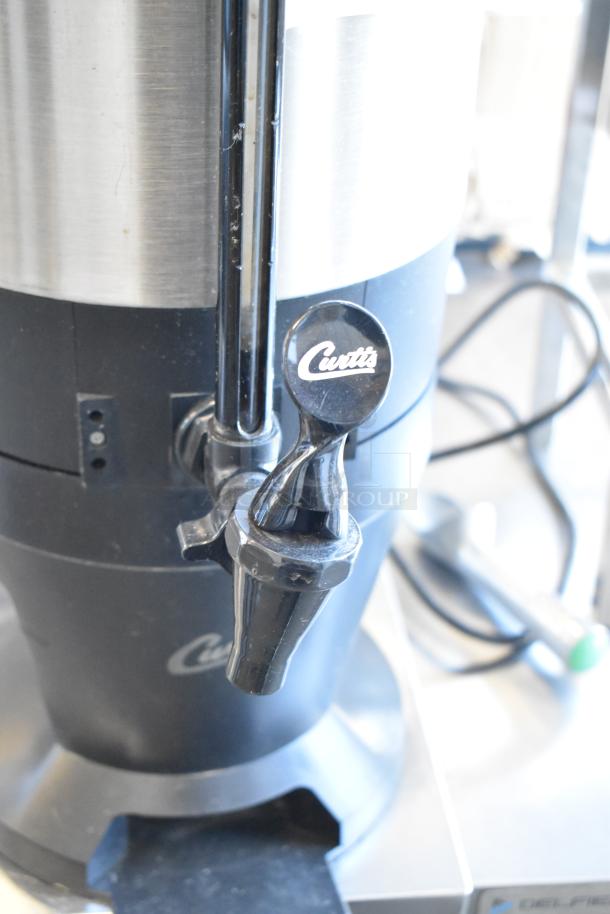 Curtis TXSG1501S600 stainless steel beverage holder dispenser with tap, clean condition, black accents, Curtis branding visible.
