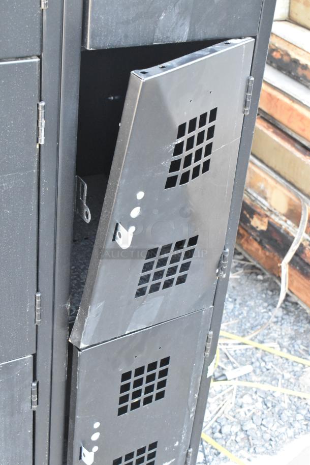 Black metal 12 cubby locker with vented doors. Some wear is visible on the surface, indicating a used condition.
