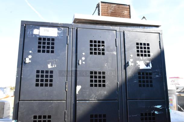 Black metal 12 cubby locker with vented doors and visible markings. Used condition with minor surface wear.