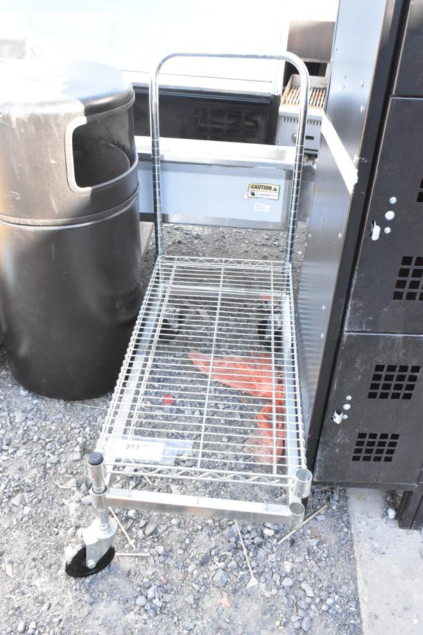 Chrome finish dunnage rack on commercial casters, missing one caster. Includes caution label, ideal for storage and transport.