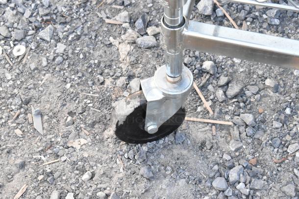 Chrome finish dunnage rack on commercial casters, one caster missing, shown on rocky ground.