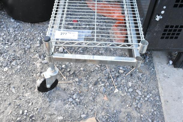 Chrome finish dunnage rack on commercial casters, one caster missing, shown on rocky ground with auction tag 277 visible.