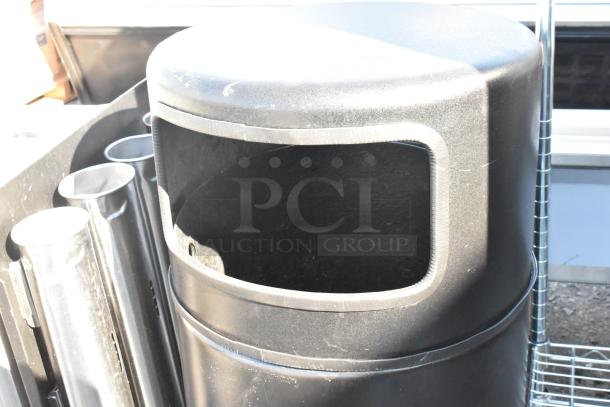 Black trash can shell with open top, cylindrical design. Made of durable material, suitable for commercial use. Good condition.