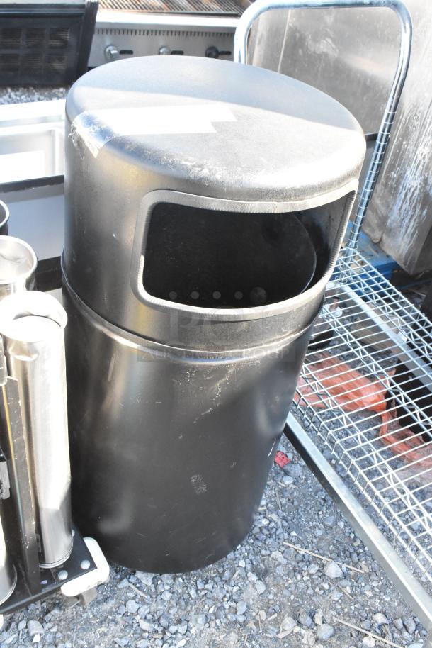 Black trash can shell in used condition, cylindrical shape, open front. Signs of wear on surface, minor scuffs visible.