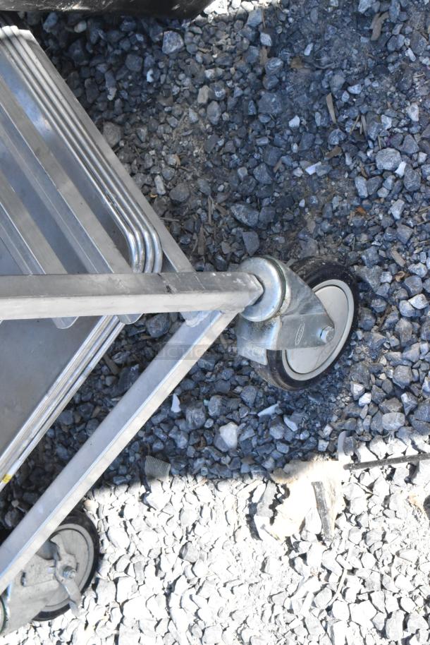 Metal commercial pan transport rack with sturdy frame and commercial casters, suitable for kitchen use. Visible signs of use.
