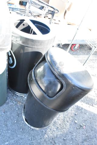 Two black trash can shells, used condition, cylindrical shape with open tops, ideal for outdoor or commercial use.
