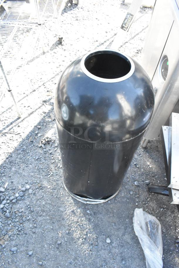 Black cylindrical trash can shell, glossy finish, open top. Some surface wear visible. Located on gravel surface.