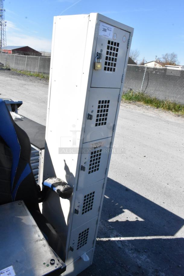 Tan metal 5 cubby locker with ventilation grilles, padlock on top cubby, and identification labels; outdoor setting.