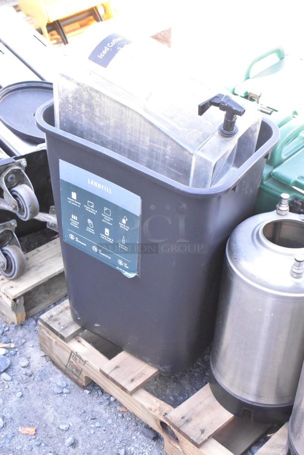 Pallet lot with metal trash can, beverage dispensers, and wet floor caution signs on a wooden pallet.