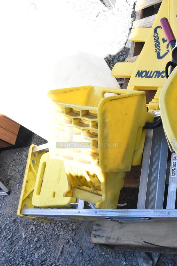 Pallet lot with yellow wet floor caution signs, metal trash can, and beverage holder dispensers, visible outdoors.