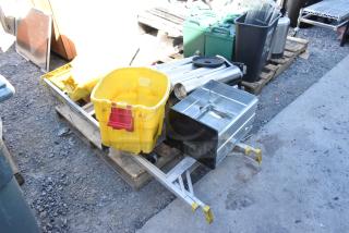 Pallet lot with ladder, yellow mop bucket, wet floor signs, and metal filing cabinet drawer on pavement.