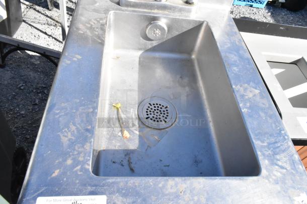 Stainless steel single bay sink, used condition, with integrated drain and faucet holes. Visible wear and debris present.