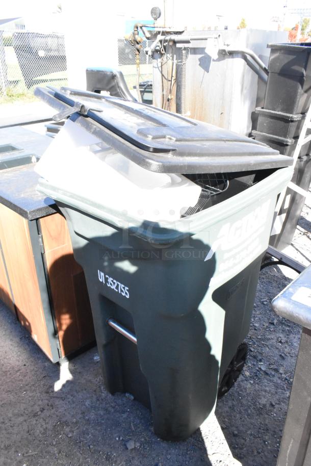 Green poly trash can with contents, partially open lid. Markings: "U7 352755" and company label visible.