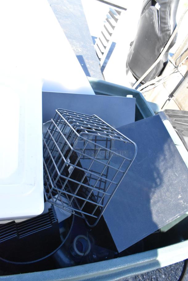 Green poly trash can with assorted contents including a metal wire basket, plastic lid, and various materials. Items visible.