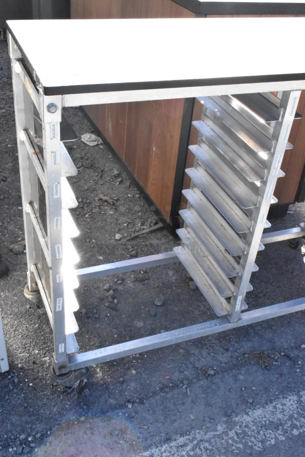 Metal commercial pan transport rack with multiple slots, labels for bagels and loaves, on sturdy commercial casters.
