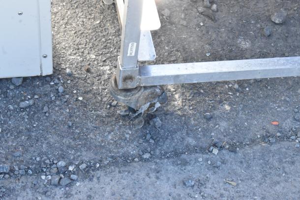 Metal commercial pan transport rack with commercial casters, shown on outdoor pavement. Visible label reads "Muffins."