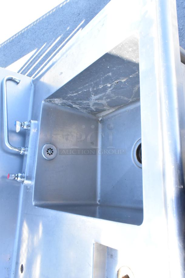 Stainless steel single bay sink with counter, back splash, and under shelf. Features dual faucets and visible strainer. Good condition.