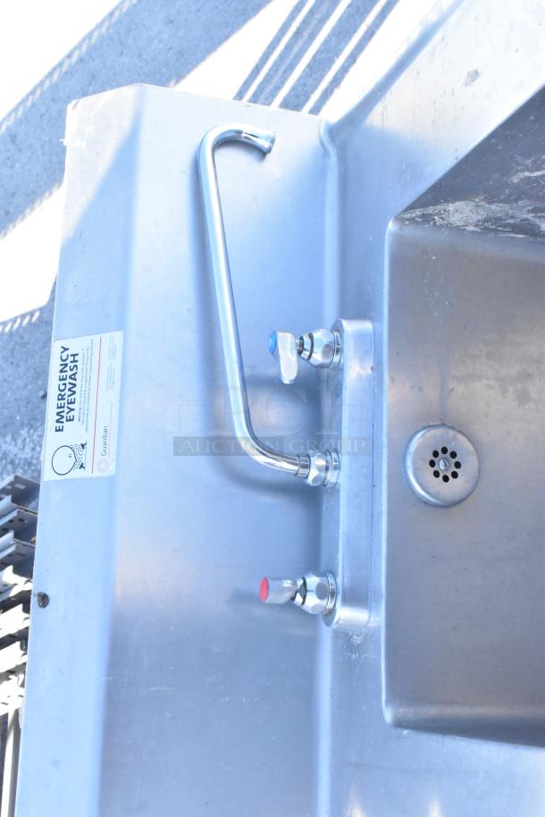 Stainless steel single bay sink with counter, backsplash, undershelf, and emergency eyewash label. Durable condition.