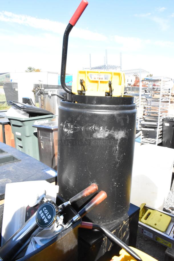 Yellow poly mop bucket on a pallet with other items, including trash cans. Features black and red handle, used condition.