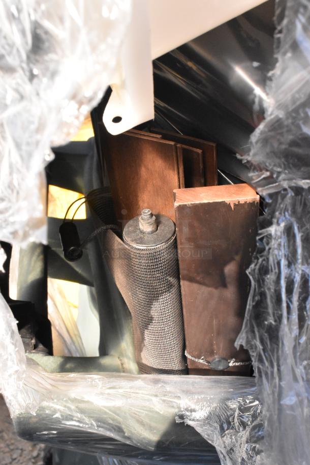 Poly trash can containing various items, including wooden planks and metal components, partially wrapped in plastic.