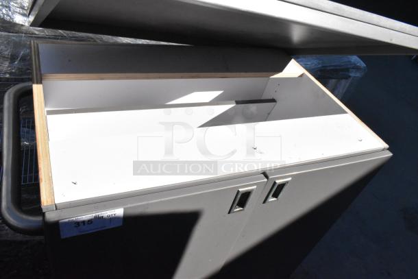 Gray 2-door cart on commercial casters, open top view, showing storage space. Tag reads "315 QTY." Durable and functional.