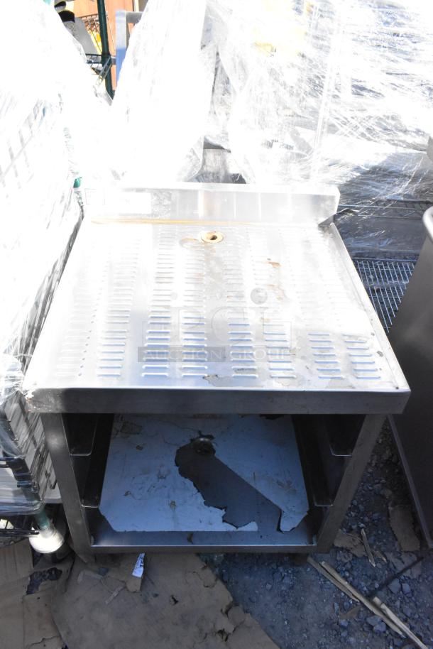 Stainless steel drain board with under shelf, features perforated top and signs of wear. Ideal for kitchens.