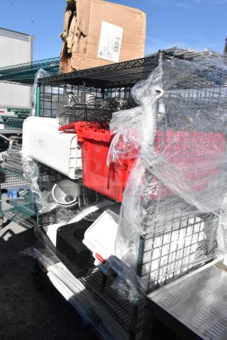 Black and green 4-tier wire shelving unit on commercial casters, contains various items, wrapped in protective plastic.