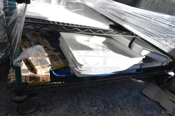 Four-tier wire shelving unit with black and green finish on commercial casters, containing trays and packaged items, in used condition.
