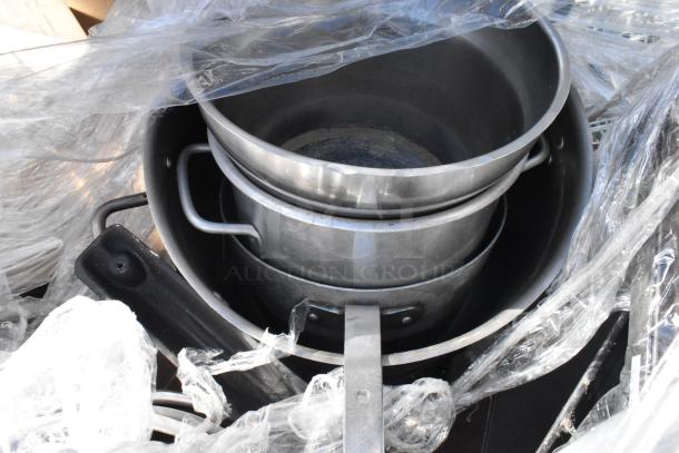 Pallet lot with various metal pots and pans, wrapped in clear plastic, featuring multiple items for auction.