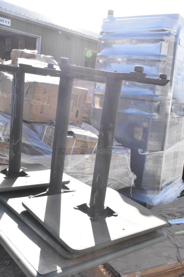 Four various tables stacked outdoors, metal legs and bases, in fair condition. Warehouse visible in background.
