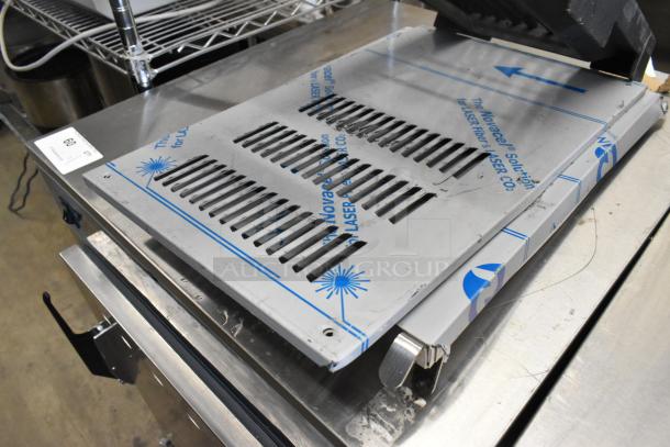 Lot of various kitchen items including a metal baking pan with ventilation slits, set on a stainless steel surface.