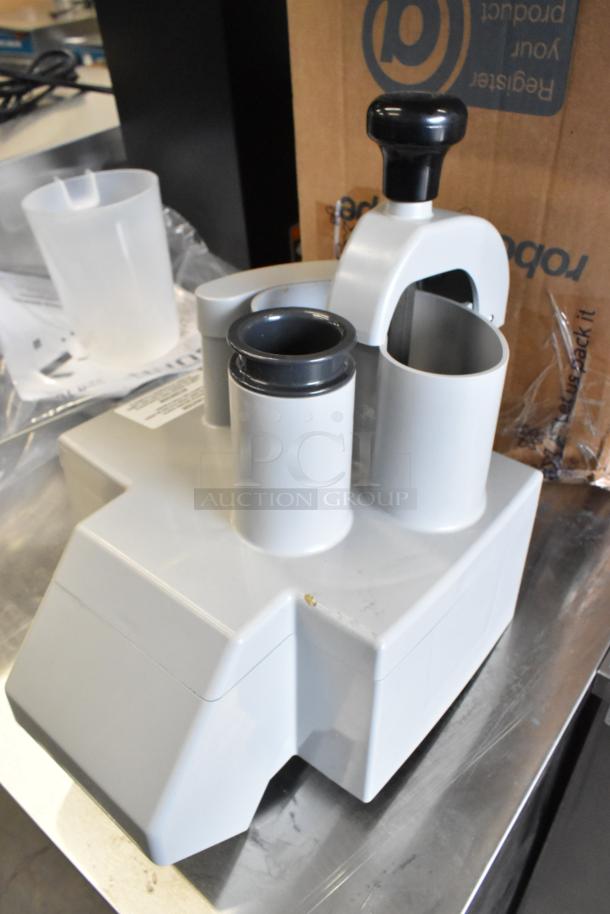 Brand new Robot Coupe 27213, slight scratch visible. Gray base, black handle, two chutes. Tags indicate model and condition.