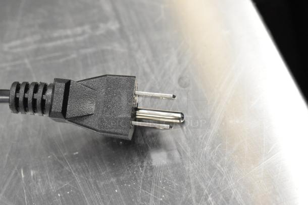 Close-up of a black power plug on a stainless steel surface, part of the AvaMix 928CJ1400 CJ1400 citrus juicer, 120V.