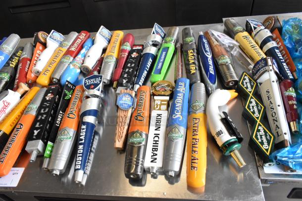 55 assorted beer tap handles, including Samuel Adams, featuring various brands and designs, showcased on a table.